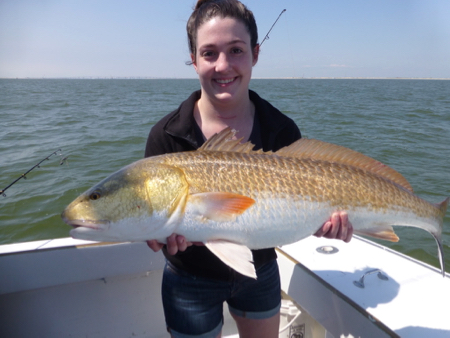 young woman dressed in black smiling holding a 40lb red drum or redfish. the fish was released back into the ocean