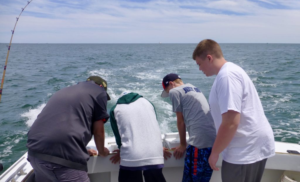 Four young boys looking into the fishbox on a summer day. Calm blue waters in the background