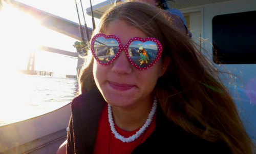 Young girl smiling with red heart shaped sunglasses catches the reflection of the water and bridges as we enter the ocean area