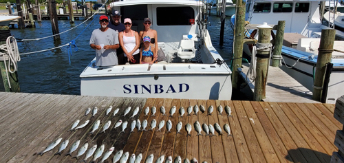 family of four standing in the boat with rows of bluefish on the dock