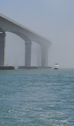 foggy morning with haze around a high bridge. a sport boat slowly moves along the bridge. you can feel the wet mist