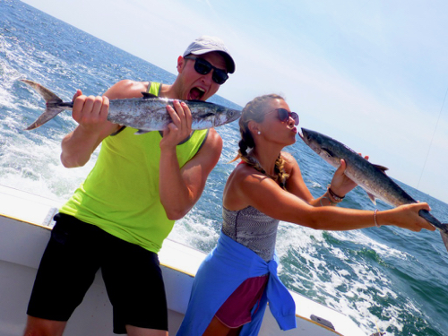 brother and sister in their twenties. goofy faces puckering to kiss fish in the sunshine on the boat