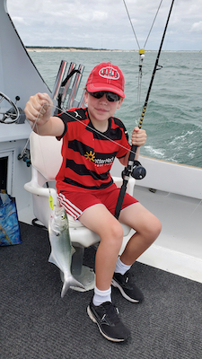 boy dressed in red ball cap and striped black and red shirt holding a fishing rod and bluefish he will release