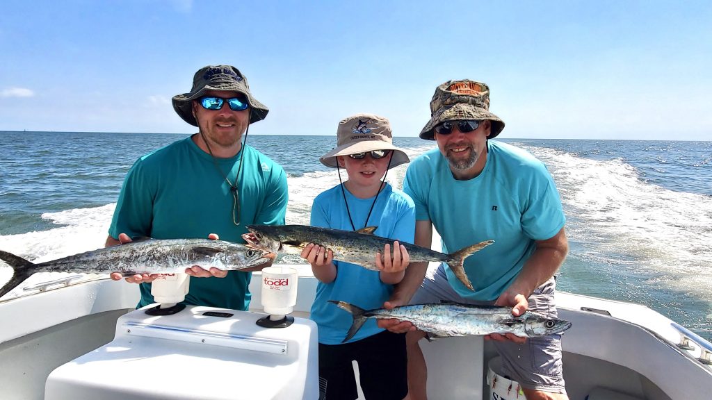Father , son, and brother all holding mackeral fish. sunny day, blue water in a white boat cockpit. all smiles. 