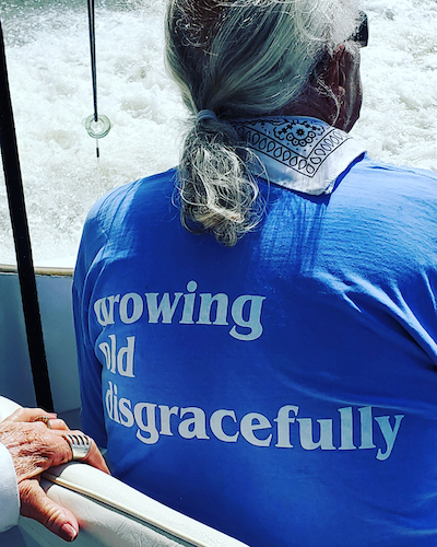 A gentlemen with gray hair in a pony tail and a t shirt back that says "growing old disgracefully"