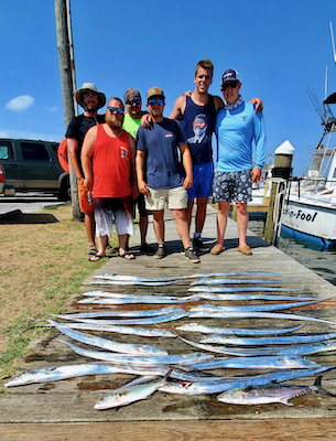 six men smiling with a dock full of silver sided metallic ribbon fish. very long , eel like fish. sunny day. 