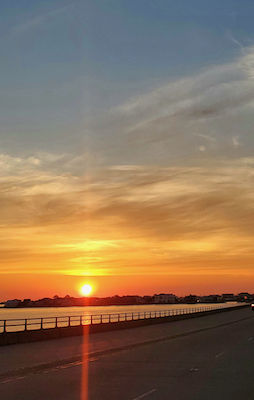  a beautiful orange sunrise on a bridge shinning on the flat bay waters