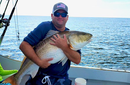 a happy man hugging a 50 pound red drum and then releasing it. the drum looks like a big orange gold fish!