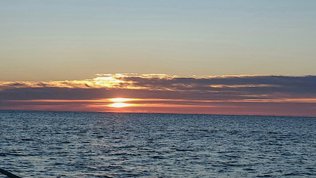 orange and gray sunrise over the calm atlantic ocean. the clouds hide the light but soon it will be daylight.