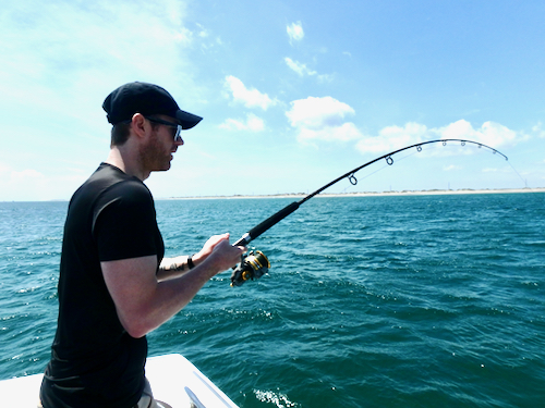 man in a black short sleeved shirt standing with a bowed over spinning rod on a blue ocean