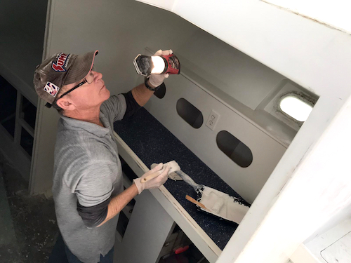 captain Will in his ball cap and painting clothes. holding a light and a paint brush in the below section of our boat. 