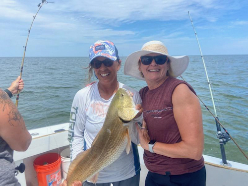 two women smiling holding a small redfish for release to the ocean. 