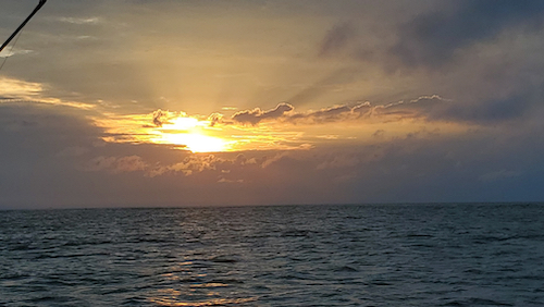 calm ocean at daybreak with sun peeking through the clouds.