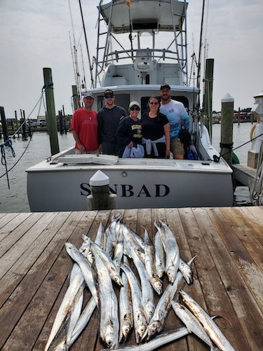 two groups of anglers in two photos. standing on the dock and cockpit with their catches of ribbon fish